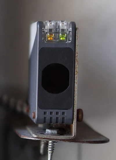 Professional garage door technician adjusting and aligning photo-eye safety sensors at garage door base, showing expert sensor repair work including wiring inspection, beam alignment, and safety system calibration to prevent random reversals for Cincinnati homeowners