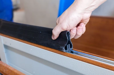 Professional garage door technician installing new bottom weather seal and perimeter rubber weatherstripping, showing expert seal replacement service to prevent drafts, water infiltration, pest entry, and improve energy efficiency for Cincinnati residential properties